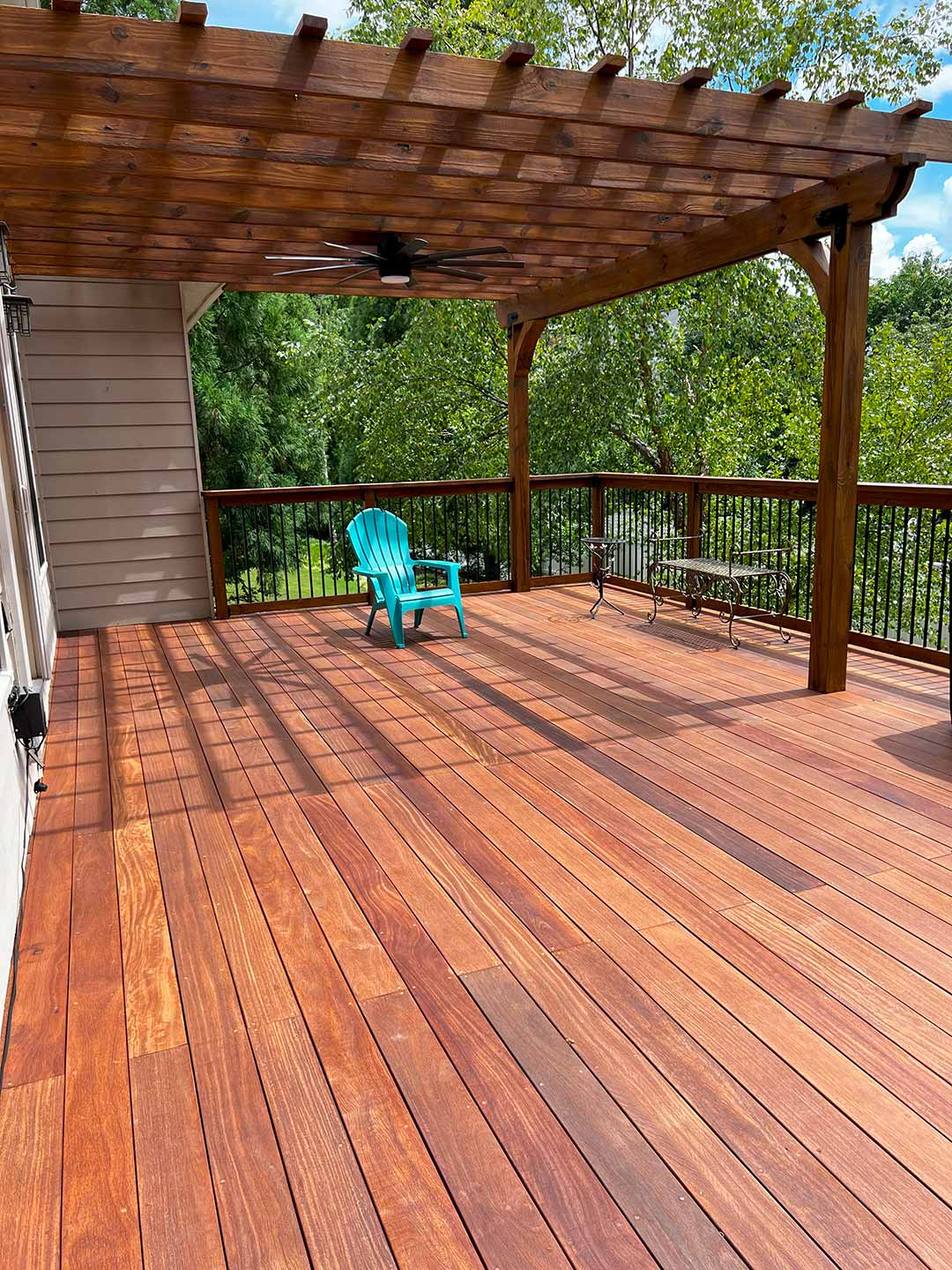 A spacious wooden deck with a pergola overhead and a single blue Adirondack chair placed near the center. This inviting space is perfect for relaxing, with trees and greenery visible in the background, making it one of the most serene decks to enjoy nature.
