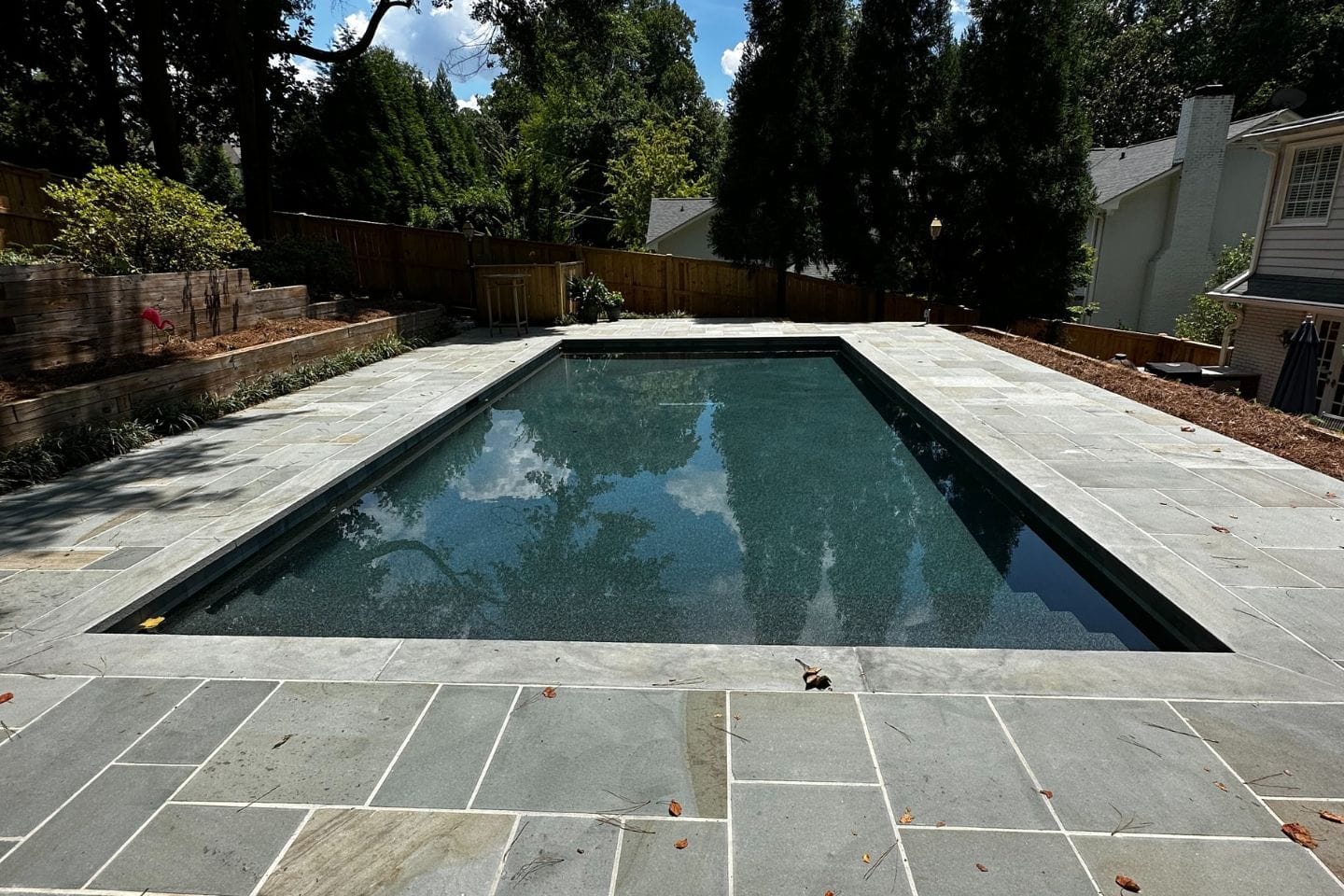A rectangular outdoor swimming pool, expertly crafted by Atlanta hardscape contractors, is surrounded by elegant stone tiles and lush greenery.