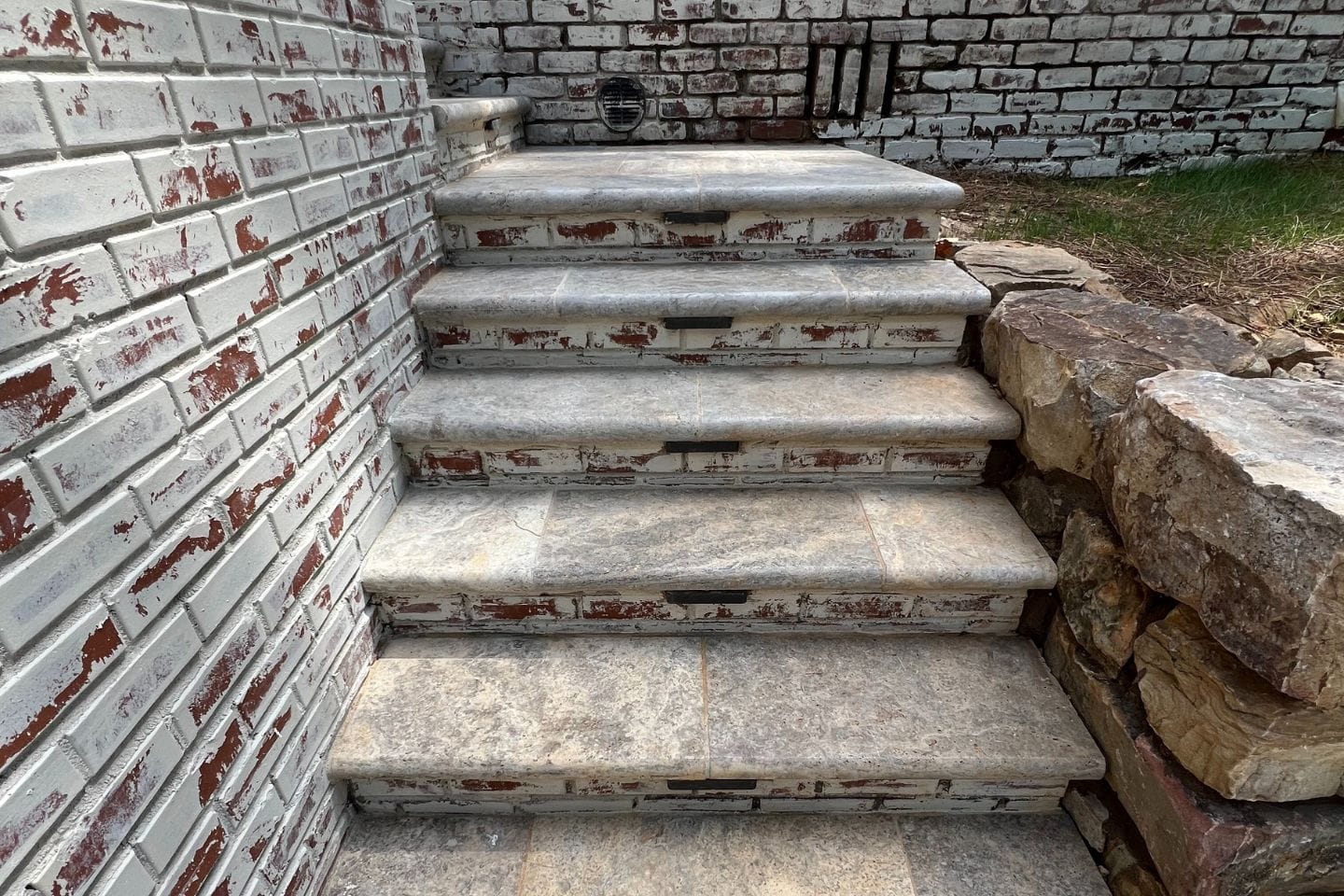Stone steps, crafted by skilled Atlanta hardscape contractors, lead up against a painted brick wall, with rocks elegantly arranged to the side.