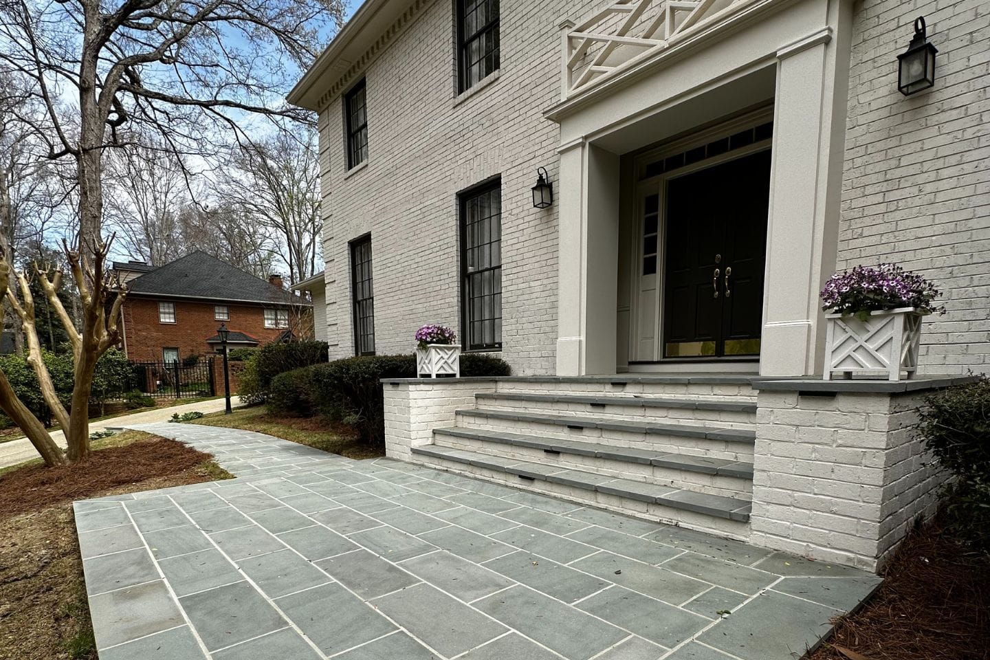 Front view of a house with a brick facade and stone steps, enhanced by the expertise of Atlanta hardscape contractors. Potted purple flowers flank the entrance, while a perfectly paved pathway invites you to the front door.