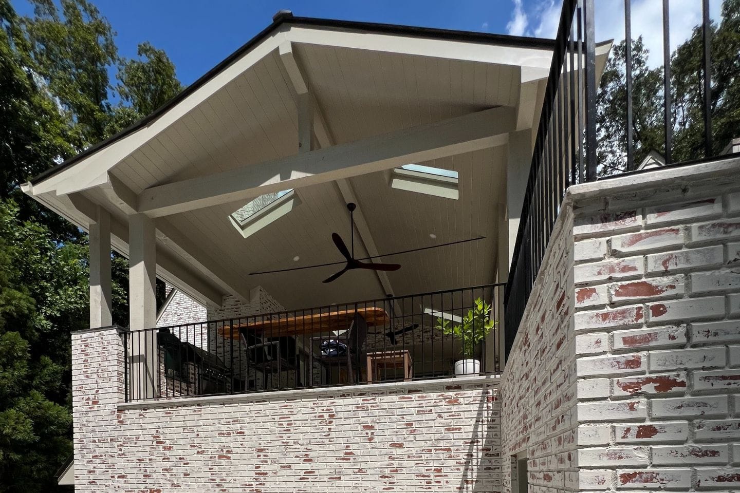 A brick building with a covered patio showcases the craftsmanship typical of Atlanta hardscape contractors, featuring a ceiling fan, skylights, and railing. A potted plant adds a touch of greenery.