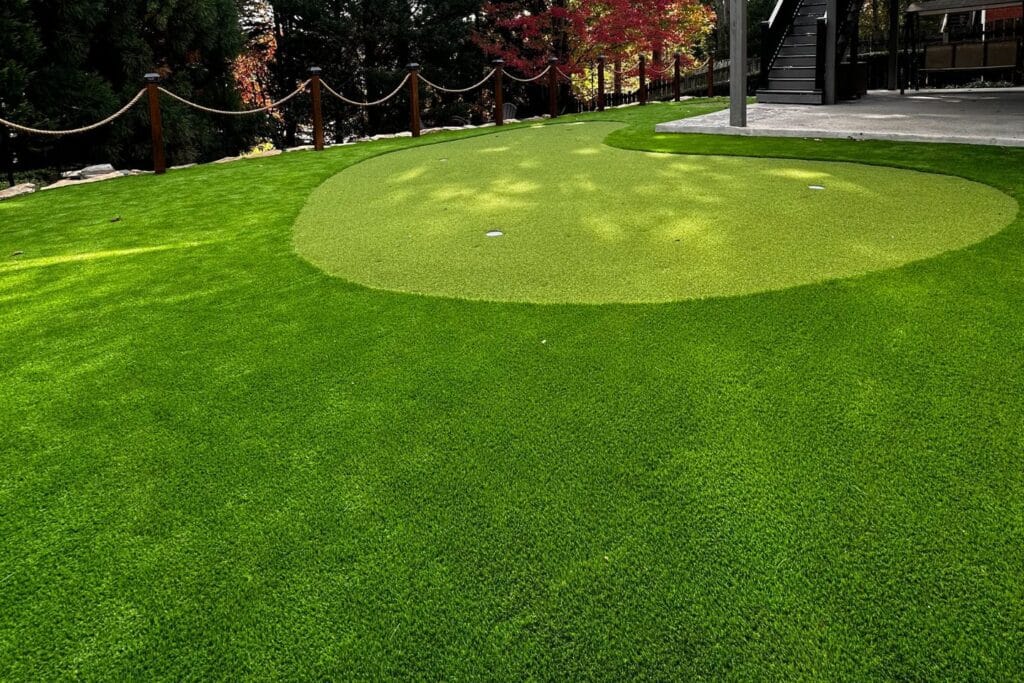 A well-maintained putting green with a small golf hole, surrounded by trees and a paved area crafted by skilled Atlanta hardscape contractors, featuring an elegant stairway.