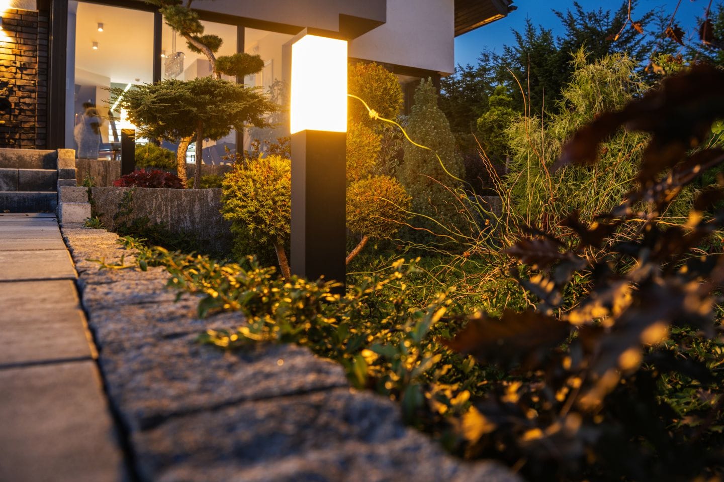 The illuminated outdoor pathway, enhanced by low-voltage lights, showcases modern garden fixtures alongside neatly trimmed plants at dusk.