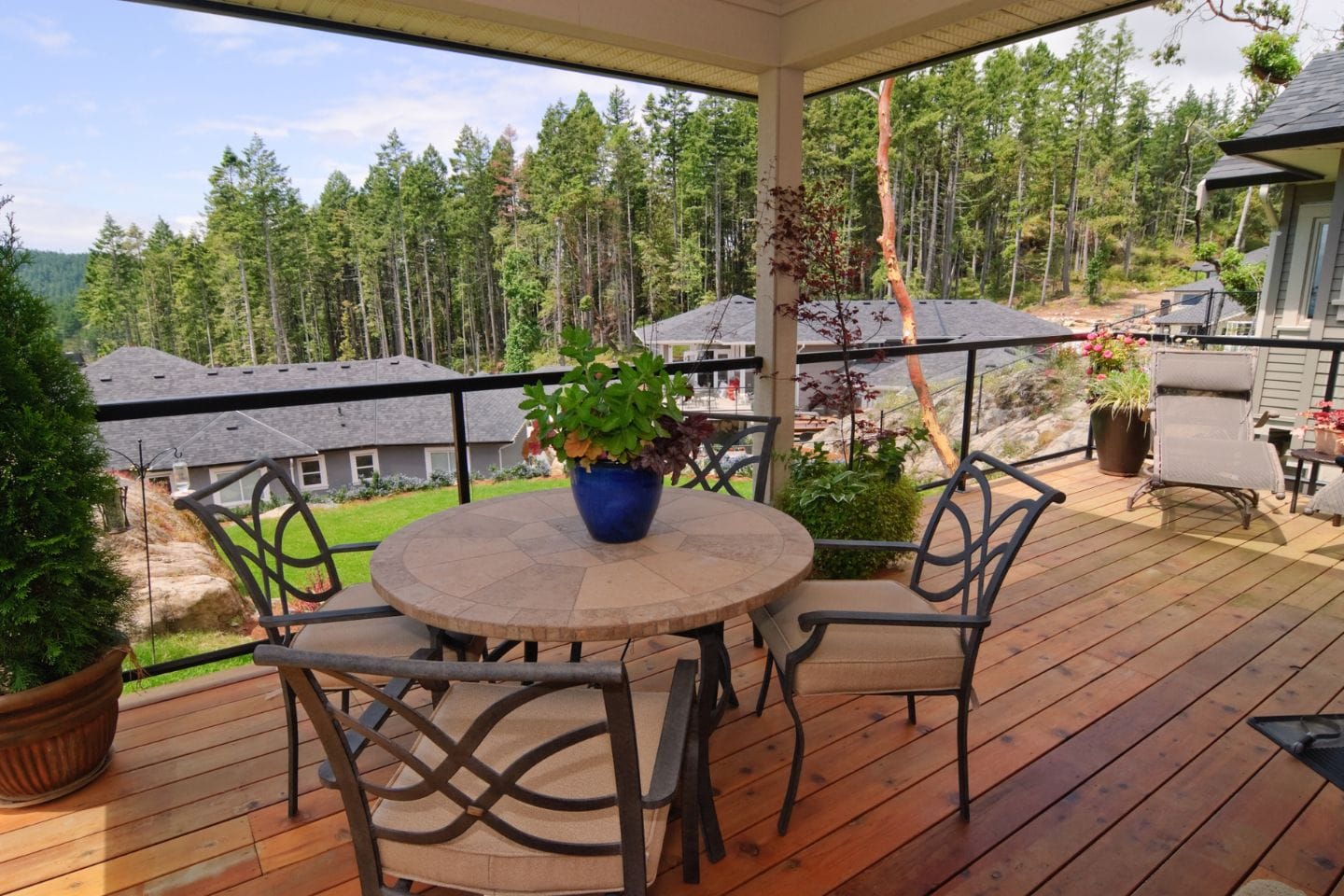 A cozy patio with a round table, four chairs, and a plant in the center overlooks decks nestled among the wooded area and nearby houses.