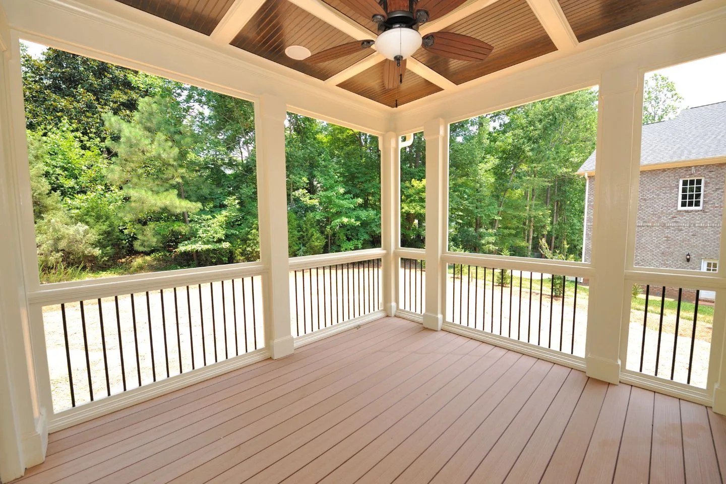 A screened porch with wooden flooring and a ceiling fan overlooks a wooded area, connecting seamlessly to the brick house, offering easy access to the adjacent decks.
