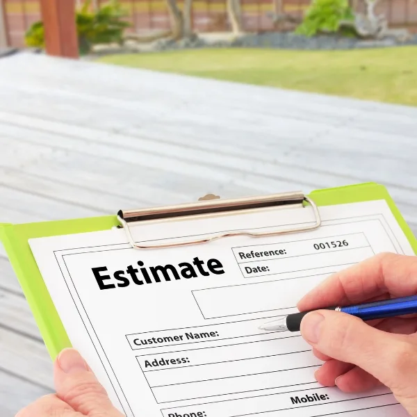 A person fills out an estimate form on a clipboard with a pen, taking careful steps next to the wooden deck.