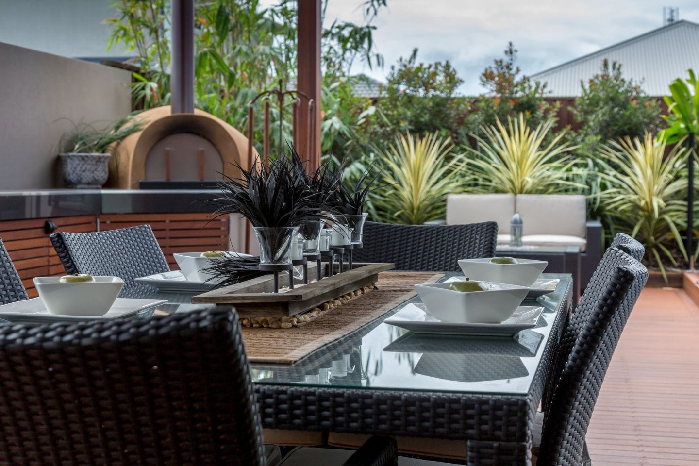 Outdoor dining area with a glass-top table, six woven chairs, and a centerpiece. The table is set with white bowls, and greenery is visible in the background. Ideal for enjoying meals while taking advantage of the beautiful surroundings and outdoor services.