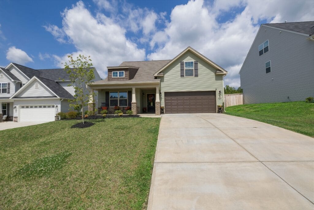 A single-family house with a double garage, beige siding, front porch, and a large driveway—perfect for exploring new driveway paving ideas—situated on a grassy lot under a partly cloudy sky.