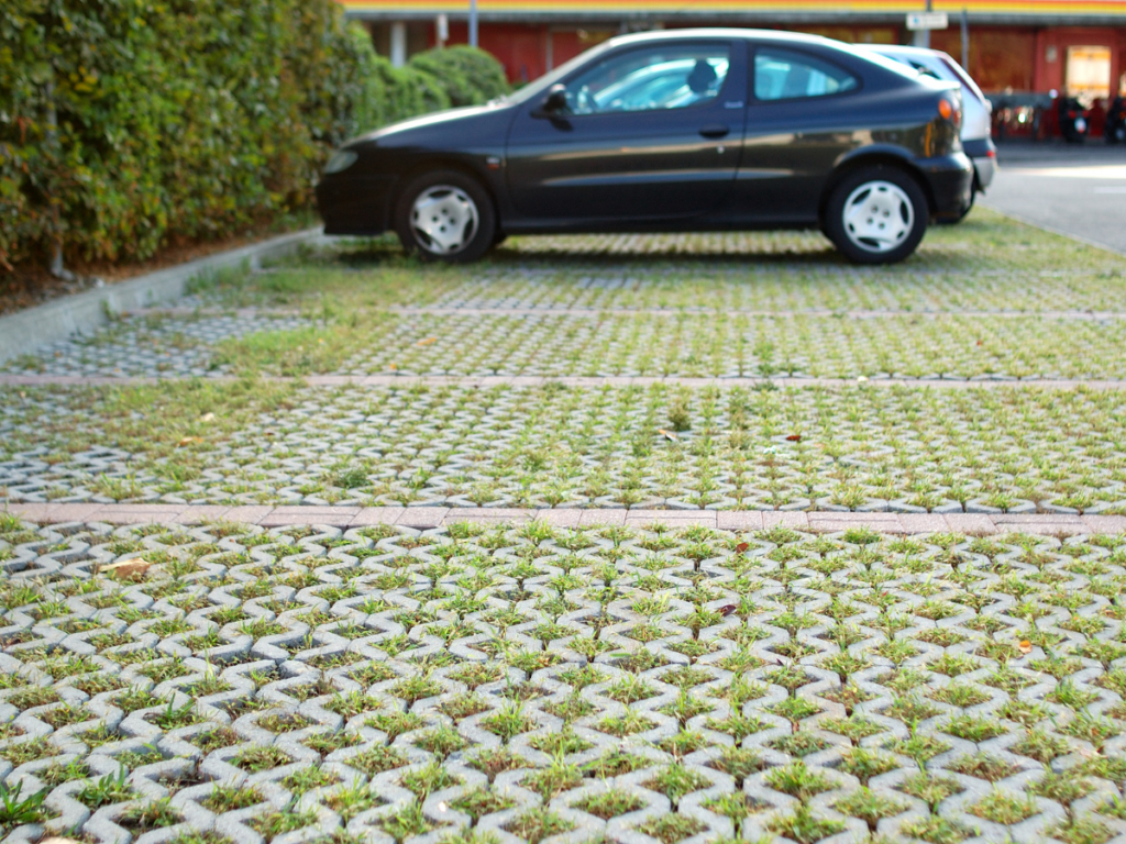 A black compact car is parked in a lot with grid-patterned paving stones featuring grass between them, highlighting natural weed control through strategic paving design.