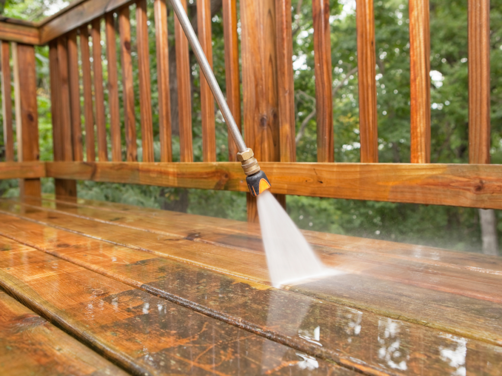 A pressure washer sprays water onto a wooden deck, pressure washing the surface and making the wood appear brighter.