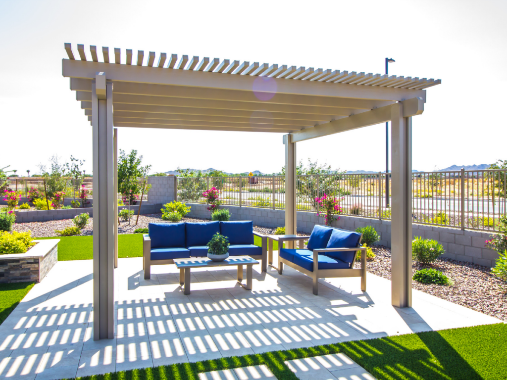 A modern pergola with blue cushioned outdoor furniture sits on a patio featuring elegant patio covers, nestled in a landscaped backyard with a fence and garden beds.